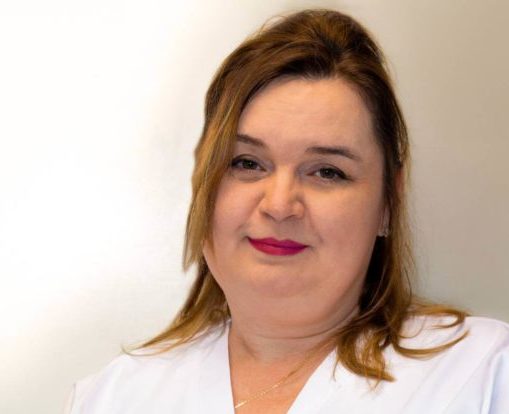 Marina Nieborak, kobieta o jasnej karnacji i brązowych włosach, ubrana w biały top, stoi na tle gładkiego, jasnego tła, patrząc w kamerę z lekkim uśmiechem. niebodent bemowo