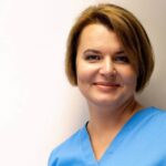 Marina Nieborak, kobieta o krótkich brązowych włosach, ubrana w niebieski strój medyczny, stoi na jednolitym, jasnym tle i delikatnie uśmiecha się do aparatu. niebodent bemowo