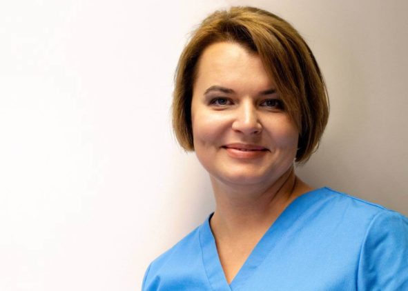 Marina Nieborak, kobieta o krótkich brązowych włosach, ubrana w niebieski strój medyczny, stoi na jednolitym, jasnym tle i delikatnie uśmiecha się do aparatu. niebodent bemowo