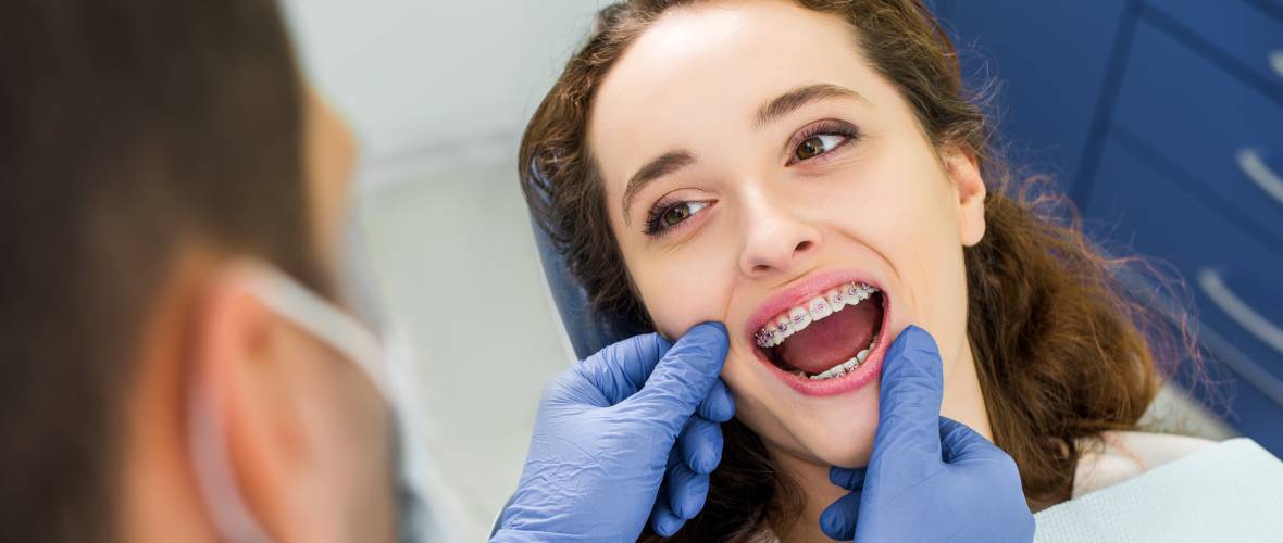 Dentysta kontroluje aparaty ortodontyczne na zębach pacjentki w gabinecie stomatologicznym.